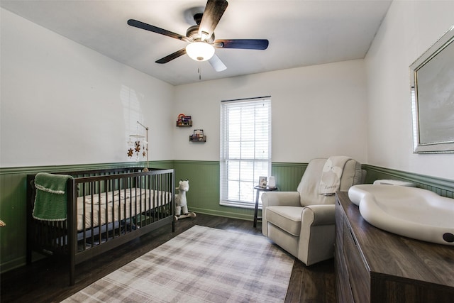 bedroom with hardwood / wood-style floors, a nursery area, and ceiling fan