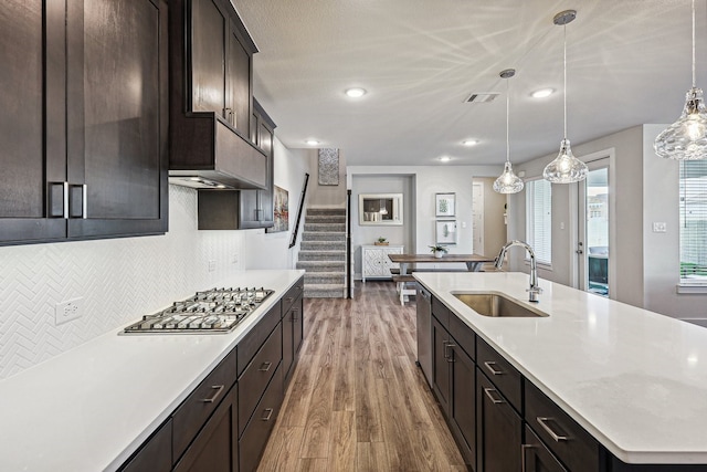 kitchen with sink, stainless steel appliances, hanging light fixtures, and an island with sink