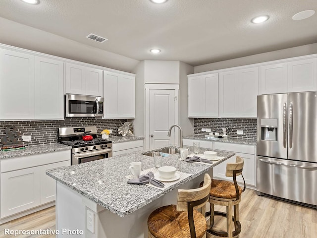 kitchen featuring a center island with sink, a breakfast bar area, stainless steel appliances, white cabinets, and sink