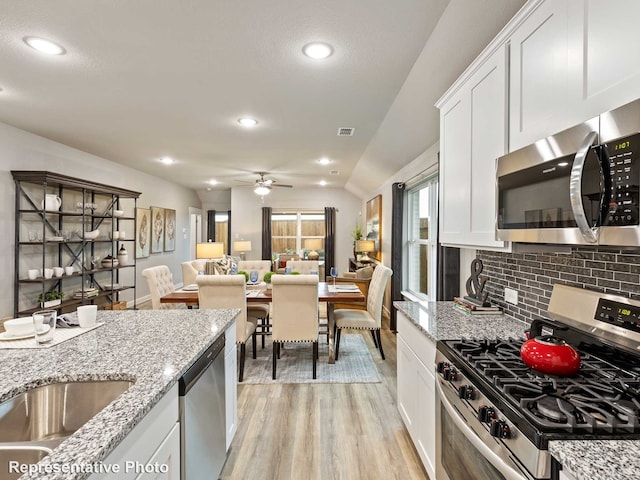 kitchen with stainless steel appliances, light wood-type flooring, light stone countertops, white cabinets, and tasteful backsplash