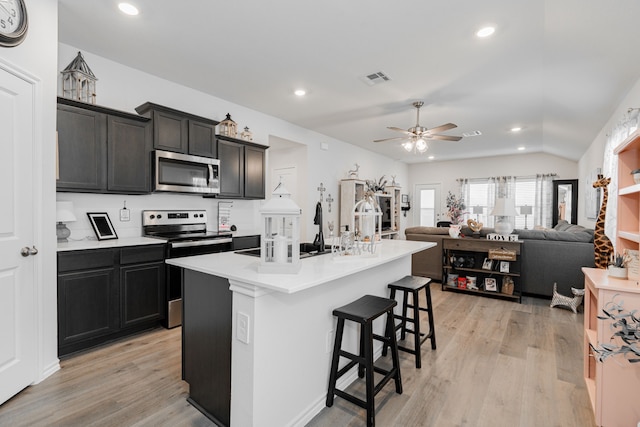 kitchen with stainless steel appliances, light hardwood / wood-style floors, a kitchen bar, a kitchen island with sink, and ceiling fan