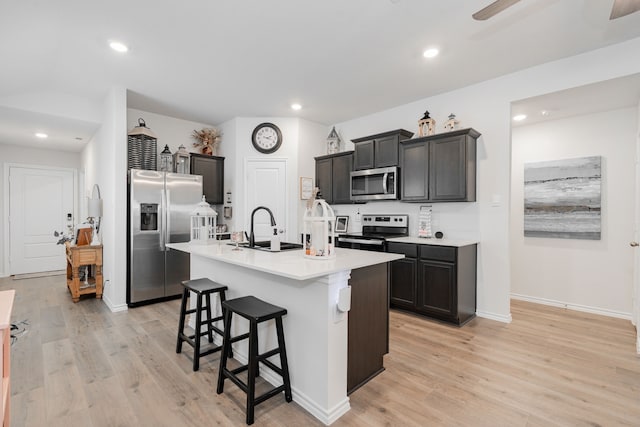 kitchen with stainless steel appliances, sink, light hardwood / wood-style flooring, an island with sink, and a breakfast bar area