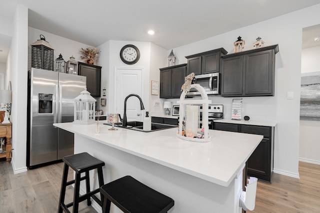 kitchen with appliances with stainless steel finishes, light hardwood / wood-style floors, a kitchen island with sink, and sink