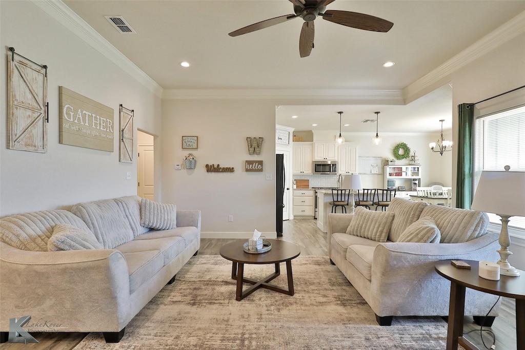 living room featuring ceiling fan with notable chandelier, light hardwood / wood-style flooring, sink, and crown molding