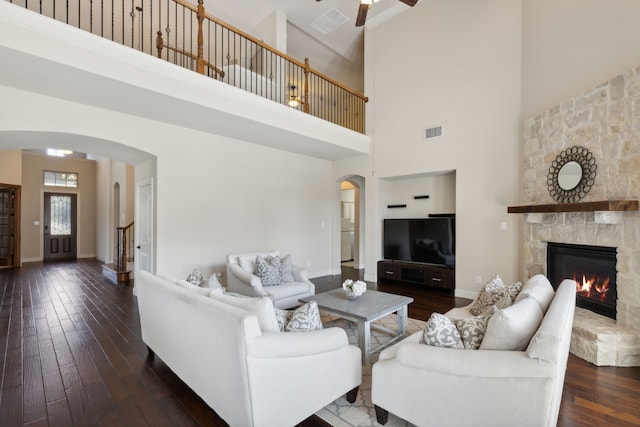 living room featuring a towering ceiling, a fireplace, ceiling fan, and dark wood-type flooring