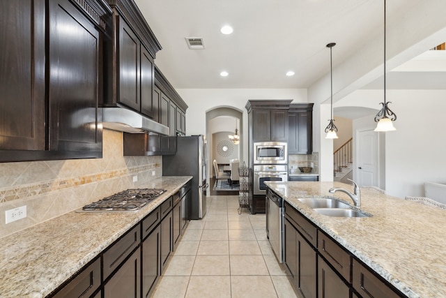 kitchen with sink, tasteful backsplash, dark brown cabinets, pendant lighting, and appliances with stainless steel finishes