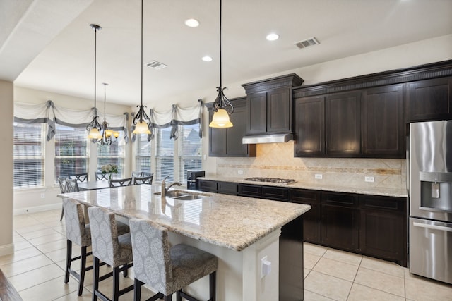 kitchen featuring stainless steel appliances, decorative light fixtures, a wealth of natural light, and a kitchen island with sink