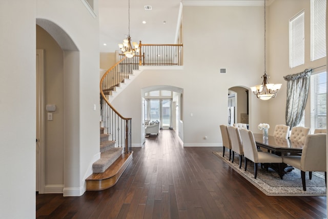 dining area featuring a towering ceiling, dark wood-type flooring, and a notable chandelier