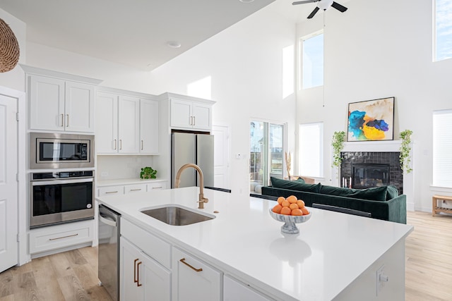 kitchen with appliances with stainless steel finishes, sink, white cabinets, a high ceiling, and a kitchen island with sink