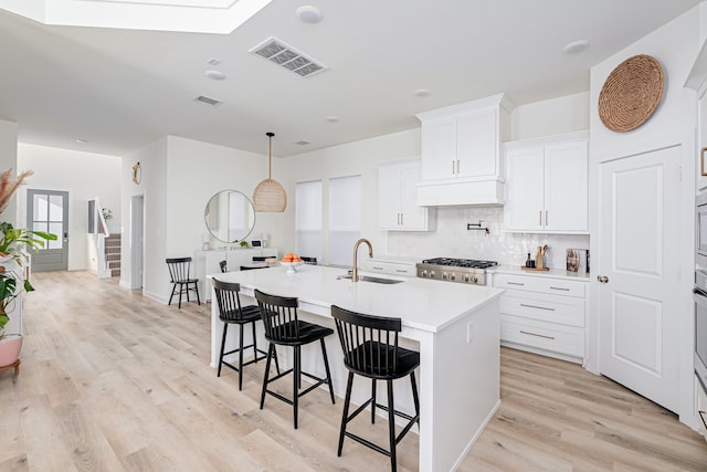 kitchen featuring sink, white cabinetry, tasteful backsplash, a kitchen breakfast bar, and an island with sink