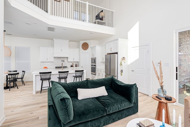 living room featuring a high ceiling, sink, and light hardwood / wood-style flooring