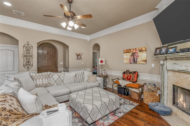 living room featuring ceiling fan, a tiled fireplace, crown molding, and wood-type flooring