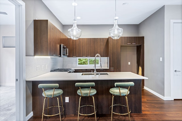 kitchen featuring dark hardwood / wood-style floors, hanging light fixtures, decorative backsplash, a kitchen breakfast bar, and sink