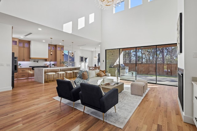 living room with a notable chandelier, light wood-type flooring, sink, and a high ceiling