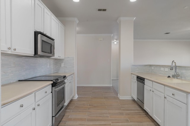 kitchen with appliances with stainless steel finishes, white cabinets, ornamental molding, and sink