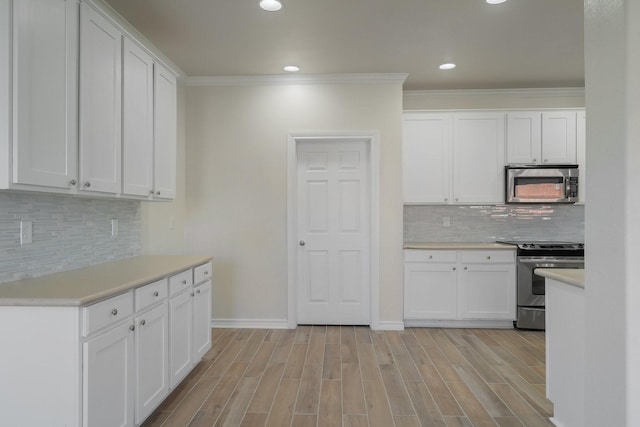 kitchen featuring appliances with stainless steel finishes, crown molding, decorative backsplash, white cabinets, and light hardwood / wood-style flooring