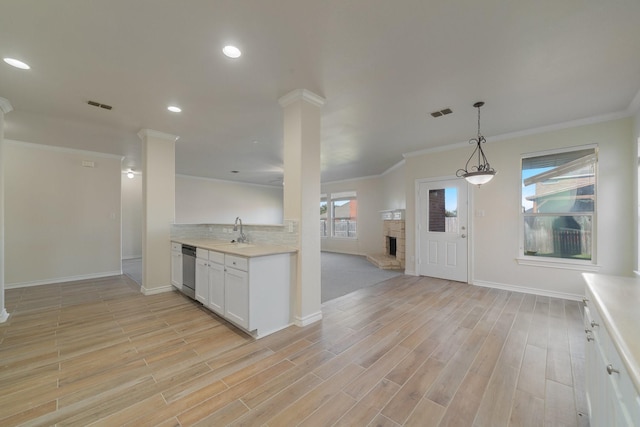 kitchen featuring a fireplace, sink, white cabinetry, decorative light fixtures, and stainless steel dishwasher