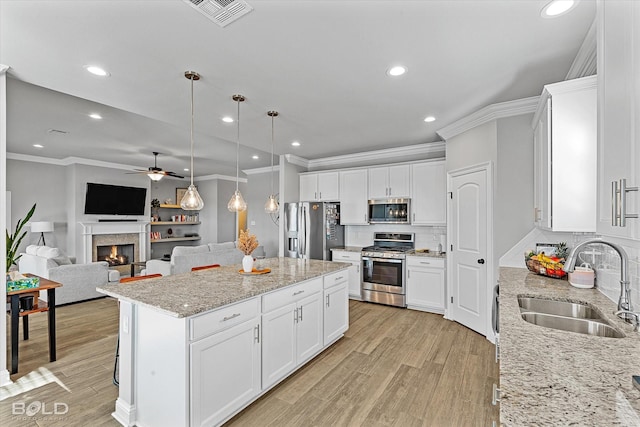 kitchen with stainless steel appliances, a center island, light stone countertops, white cabinets, and sink