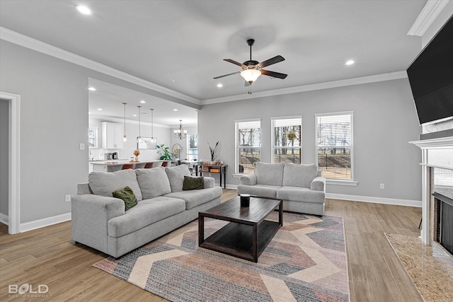 living room featuring a premium fireplace, light hardwood / wood-style flooring, crown molding, and ceiling fan with notable chandelier