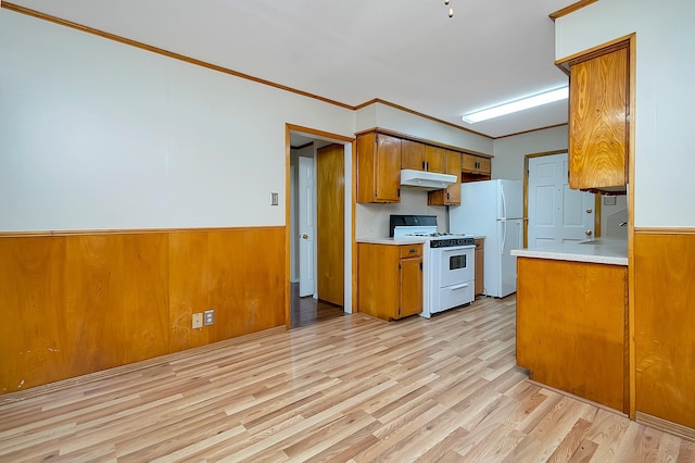 kitchen with wooden walls, white appliances, ornamental molding, and light hardwood / wood-style floors