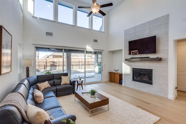 living room featuring a towering ceiling, a tiled fireplace, light hardwood / wood-style floors, and a wealth of natural light