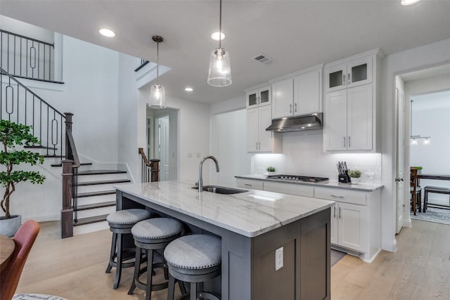 kitchen featuring sink, hanging light fixtures, white cabinets, and a kitchen island with sink