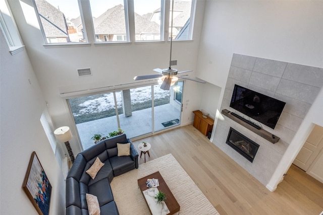 living room with a towering ceiling, a tile fireplace, ceiling fan, and light hardwood / wood-style flooring