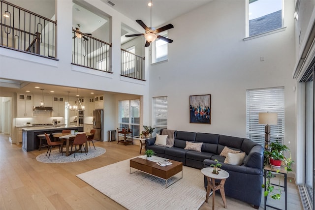 living room with ceiling fan, light hardwood / wood-style flooring, and a towering ceiling