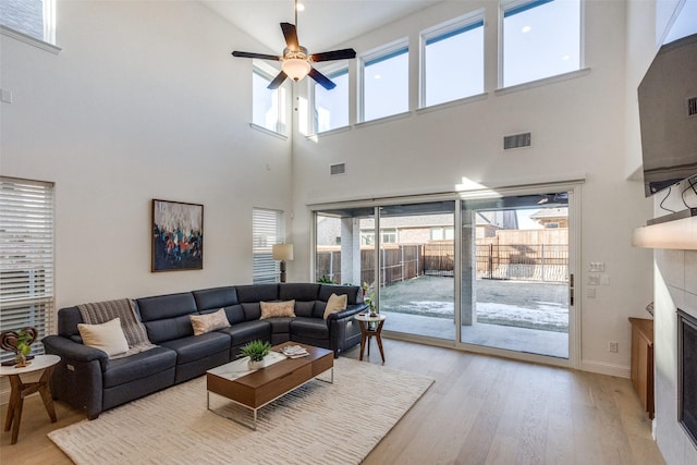 living room with a high ceiling, ceiling fan, light wood-type flooring, and a fireplace