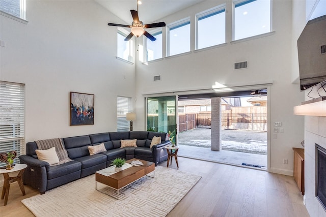 living room with ceiling fan, light hardwood / wood-style flooring, a tile fireplace, and a towering ceiling