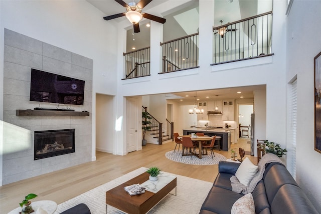 living room with light hardwood / wood-style floors, ceiling fan, a towering ceiling, and a fireplace