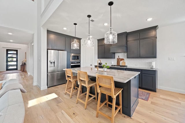 kitchen featuring a kitchen island with sink, appliances with stainless steel finishes, hanging light fixtures, a kitchen bar, and sink