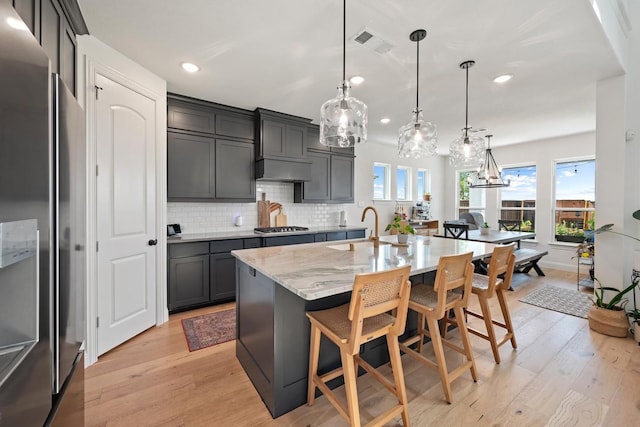 kitchen featuring decorative light fixtures, a spacious island, light hardwood / wood-style floors, a kitchen bar, and appliances with stainless steel finishes