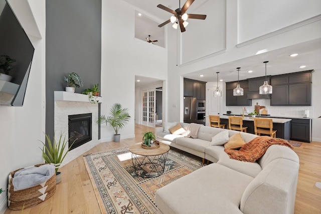 living room featuring a high ceiling, ceiling fan, and light hardwood / wood-style flooring