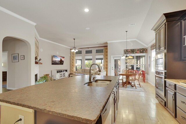 kitchen featuring stainless steel appliances, ornamental molding, vaulted ceiling, a sink, and an island with sink