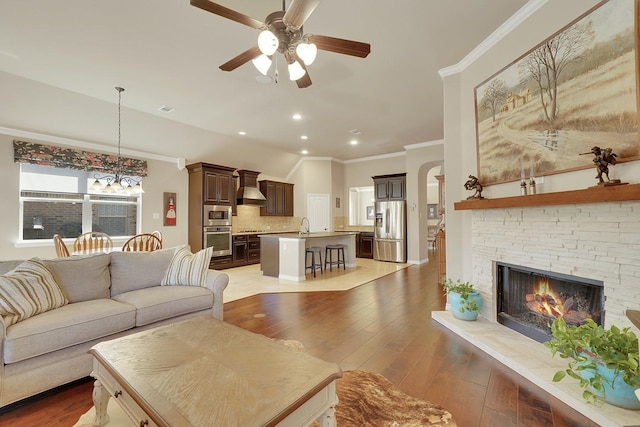 living area featuring a fireplace, light wood finished floors, recessed lighting, ornamental molding, and ceiling fan with notable chandelier