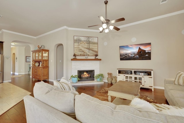 living area with arched walkways, crown molding, wood finished floors, a warm lit fireplace, and baseboards