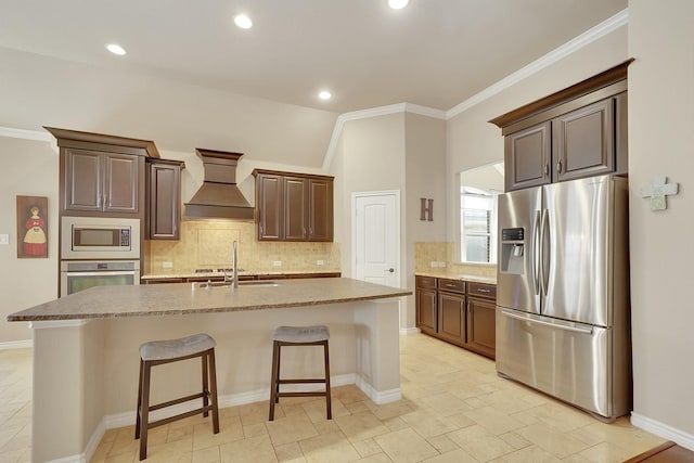 kitchen featuring tasteful backsplash, a center island with sink, a breakfast bar area, custom exhaust hood, and stainless steel appliances