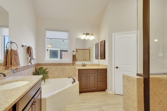 bathroom featuring lofted ceiling, two vanities, a sink, and a bath