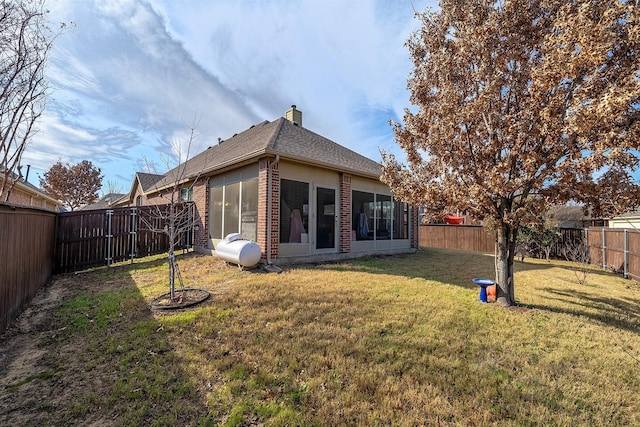 rear view of property featuring a fenced backyard, brick siding, a sunroom, a lawn, and a chimney