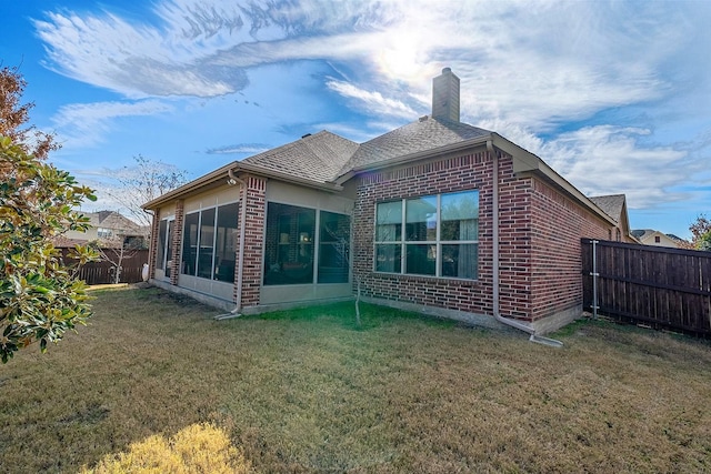 back of property featuring brick siding, a chimney, a lawn, a sunroom, and fence private yard