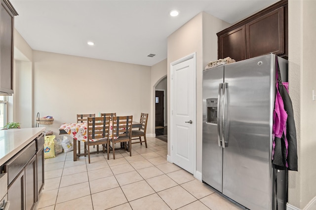 kitchen with arched walkways, stainless steel refrigerator with ice dispenser, light countertops, light tile patterned flooring, and dark brown cabinets