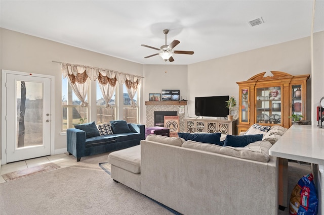 living area with ceiling fan, light tile patterned floors, light carpet, a fireplace, and visible vents