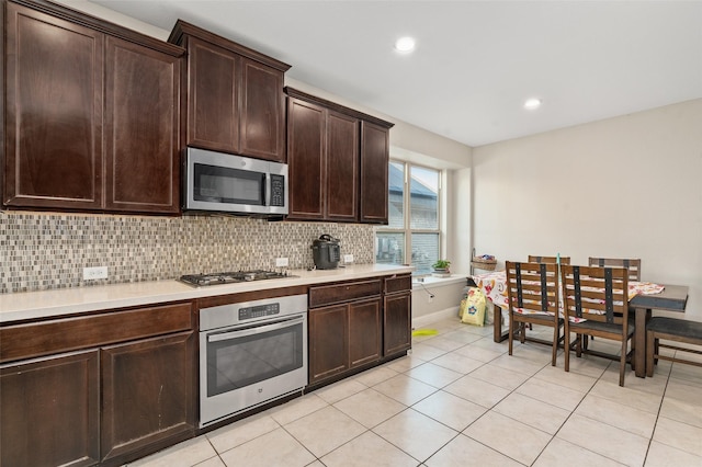 kitchen with dark brown cabinetry, light tile patterned floors, appliances with stainless steel finishes, light countertops, and backsplash