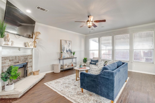 living room with a stone fireplace, ceiling fan, crown molding, and dark hardwood / wood-style floors