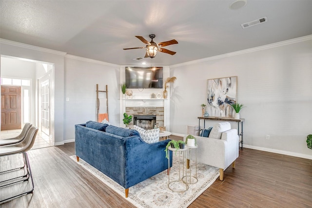 living room featuring ceiling fan, crown molding, dark hardwood / wood-style flooring, and a stone fireplace