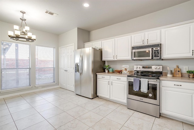 kitchen featuring decorative light fixtures, stainless steel appliances, a notable chandelier, light tile patterned floors, and white cabinetry