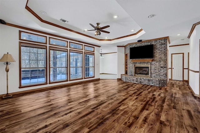 unfurnished living room with ceiling fan, hardwood / wood-style flooring, ornamental molding, a brick fireplace, and a tray ceiling