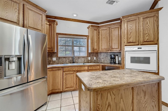 kitchen featuring sink, oven, light tile patterned floors, decorative backsplash, and stainless steel fridge with ice dispenser