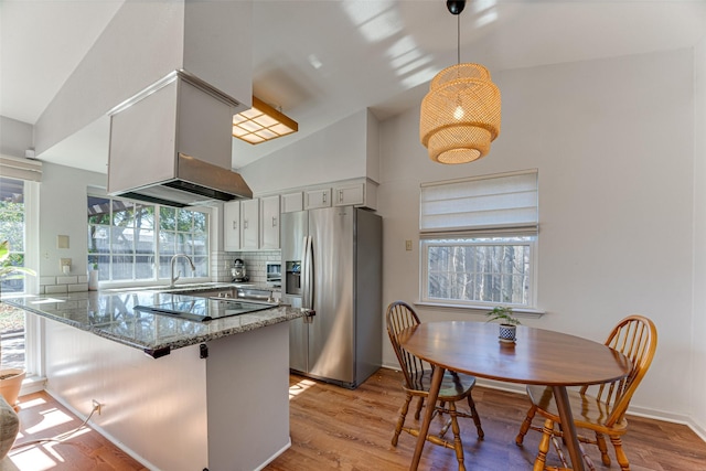 kitchen featuring stone countertops, pendant lighting, white cabinetry, stainless steel fridge, and kitchen peninsula